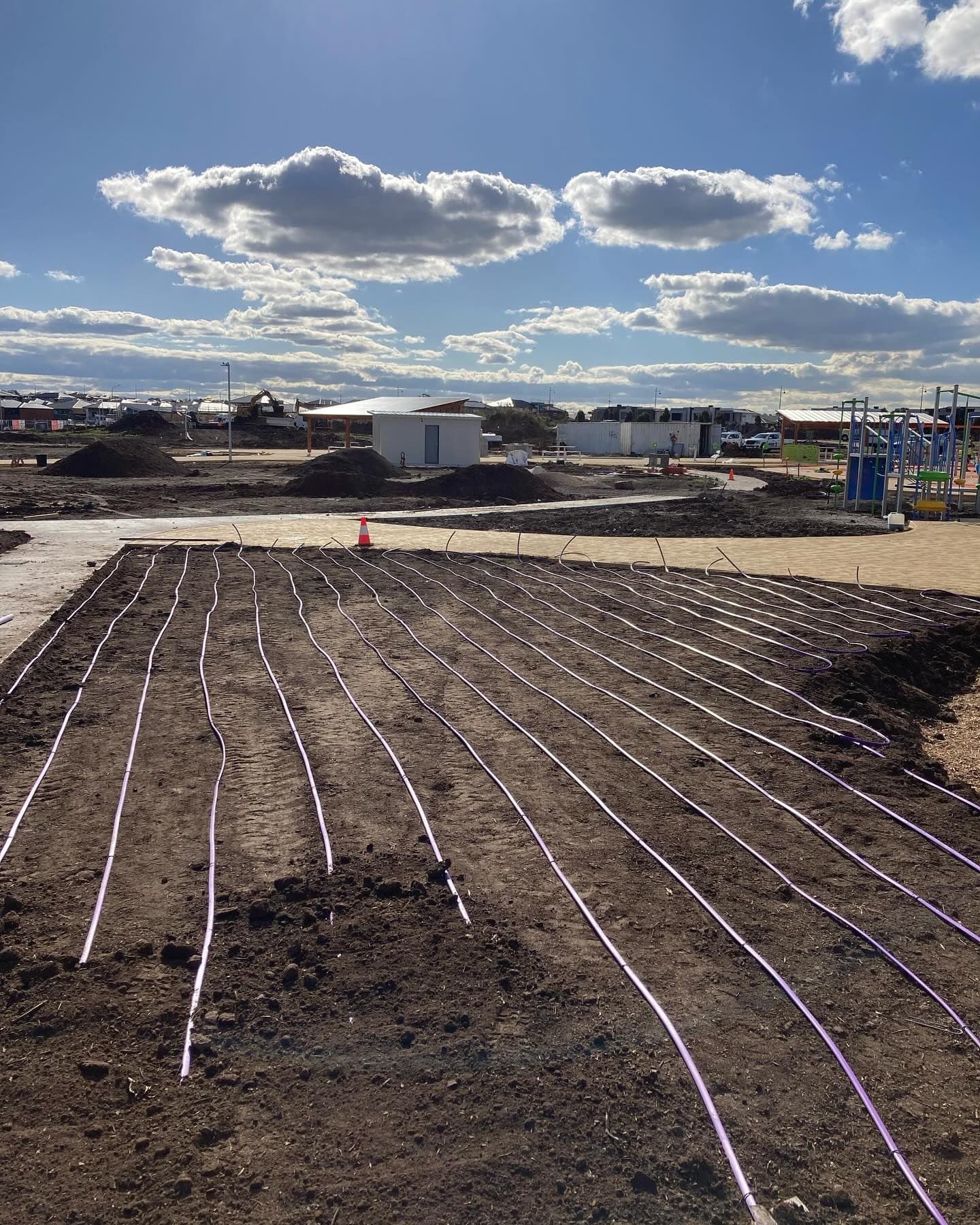 Dripline irrigation installed in the foreground with the newly constructed playspace and wider Highlands Reserve development visible behind it