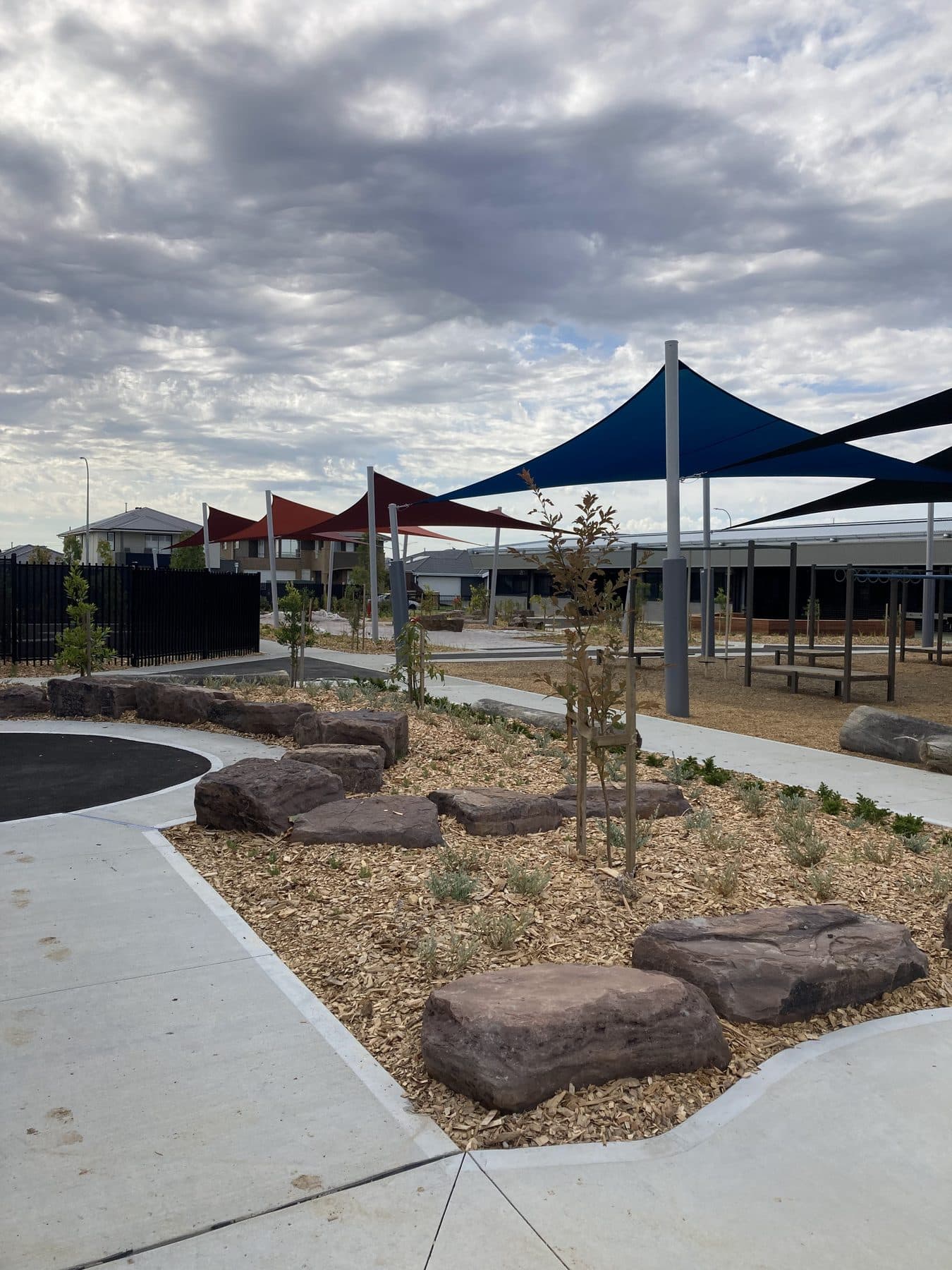 Completed school courtyard with blue and red shade sails, pathways, feature rocks and established planting